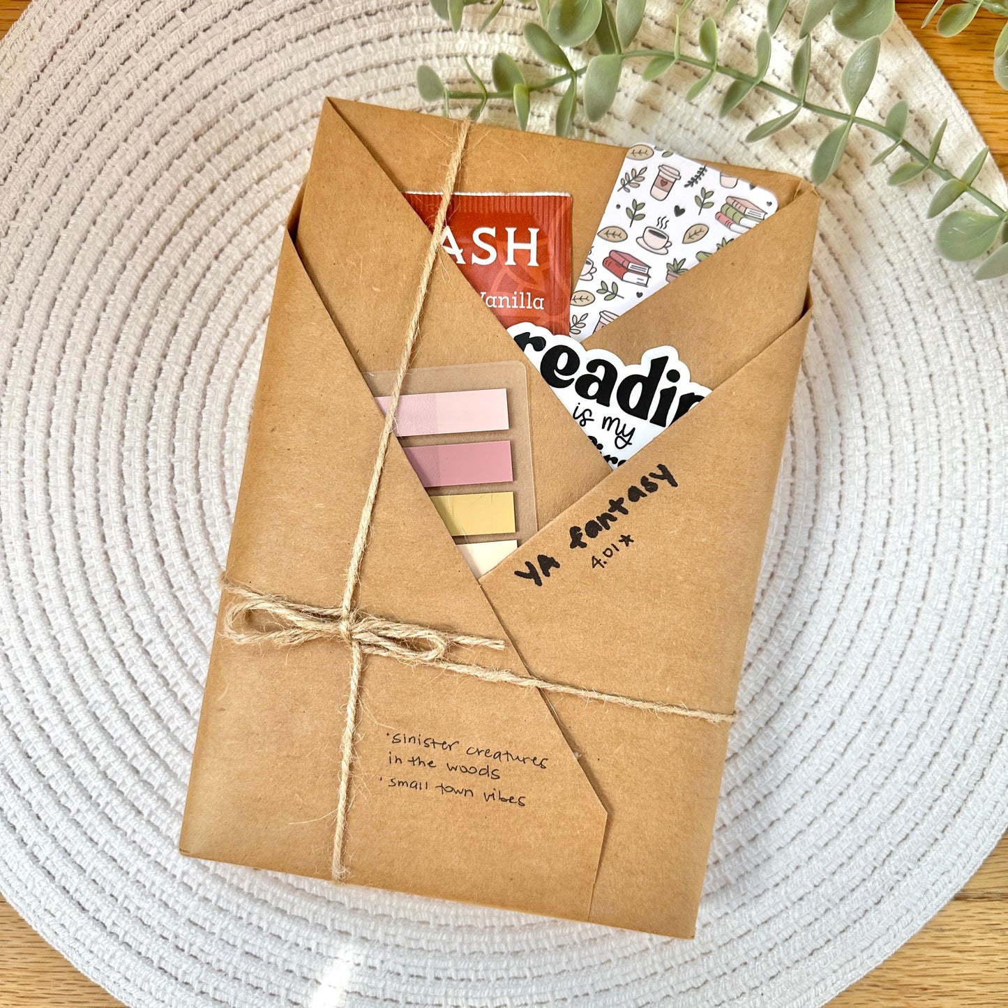 a wrapped YA fantasy book on a woven mat with decorative stationery items