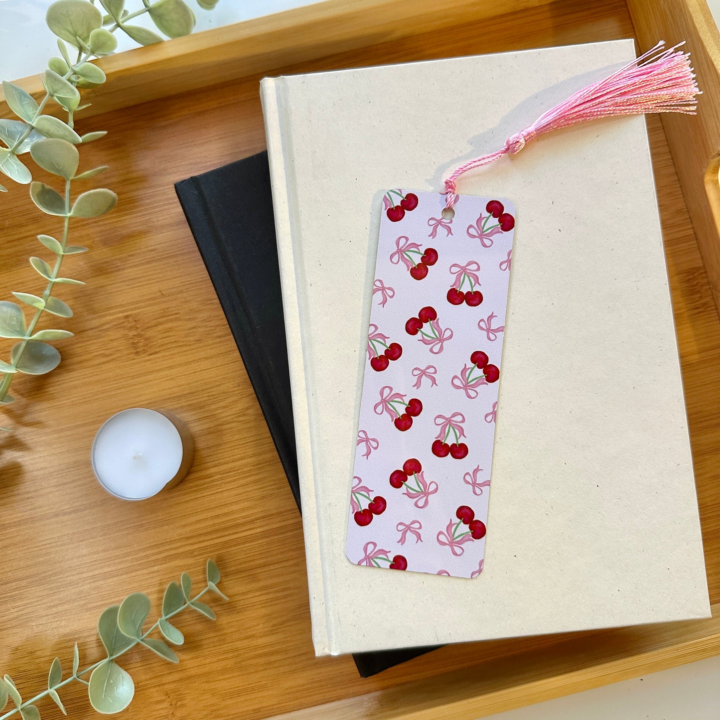 a cherries and bows bookmark on a book with a candle and greenery
