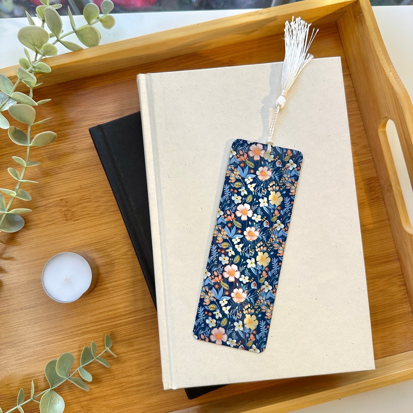 Blue floral bookmark on a book with a candle and plant