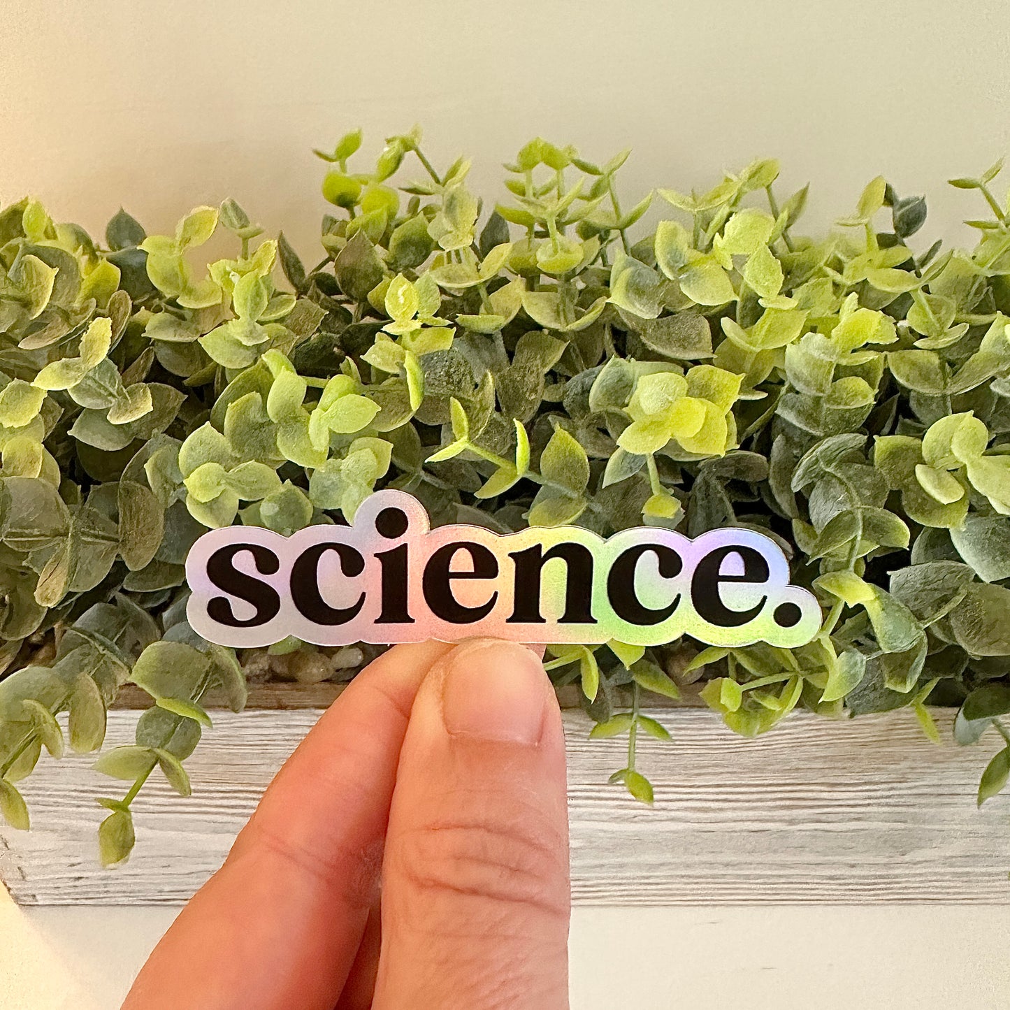 Holographic 'science.' sticker held over green leaves