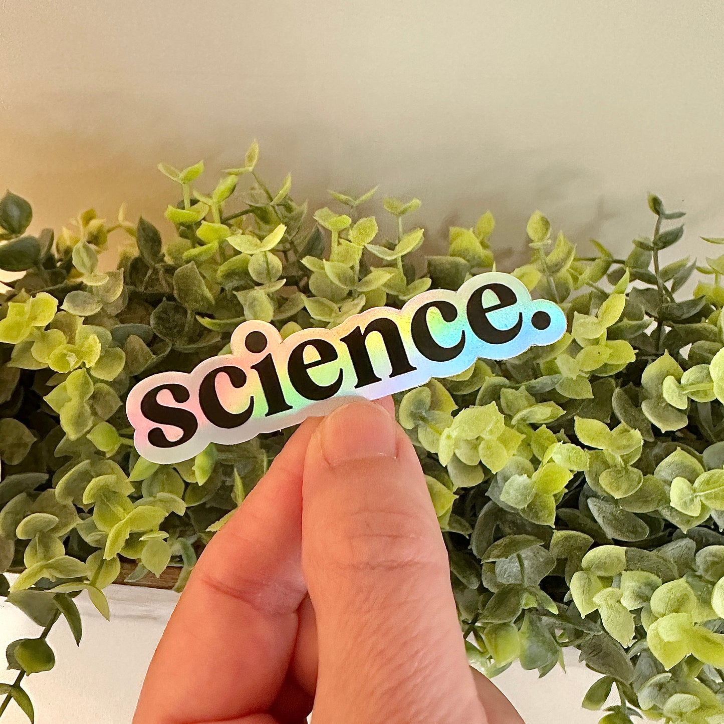 Holographic 'science.' sticker held over green leaves
