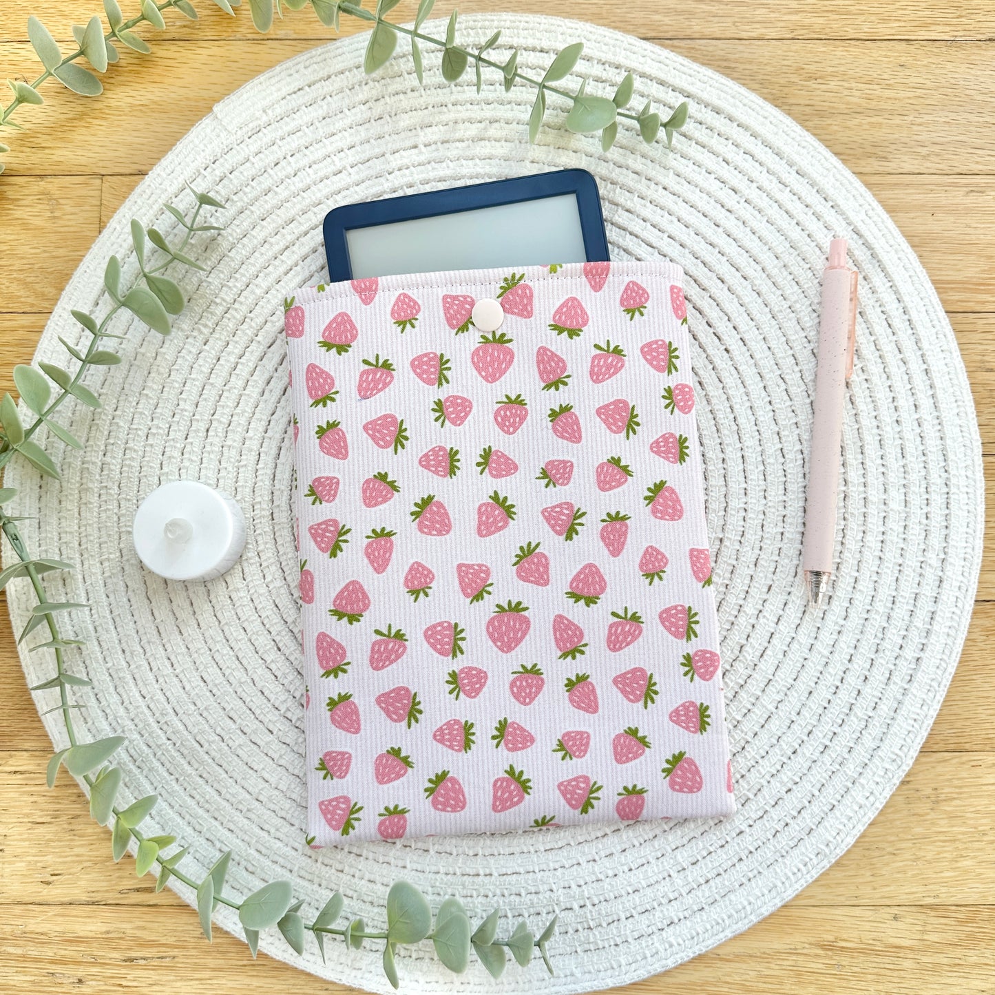 strawberry kindle sleeve on table with pen, foliage, and candle