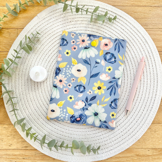 Floral-patterned kindle sleeve on a woven placemat with eucalyptus leaves.