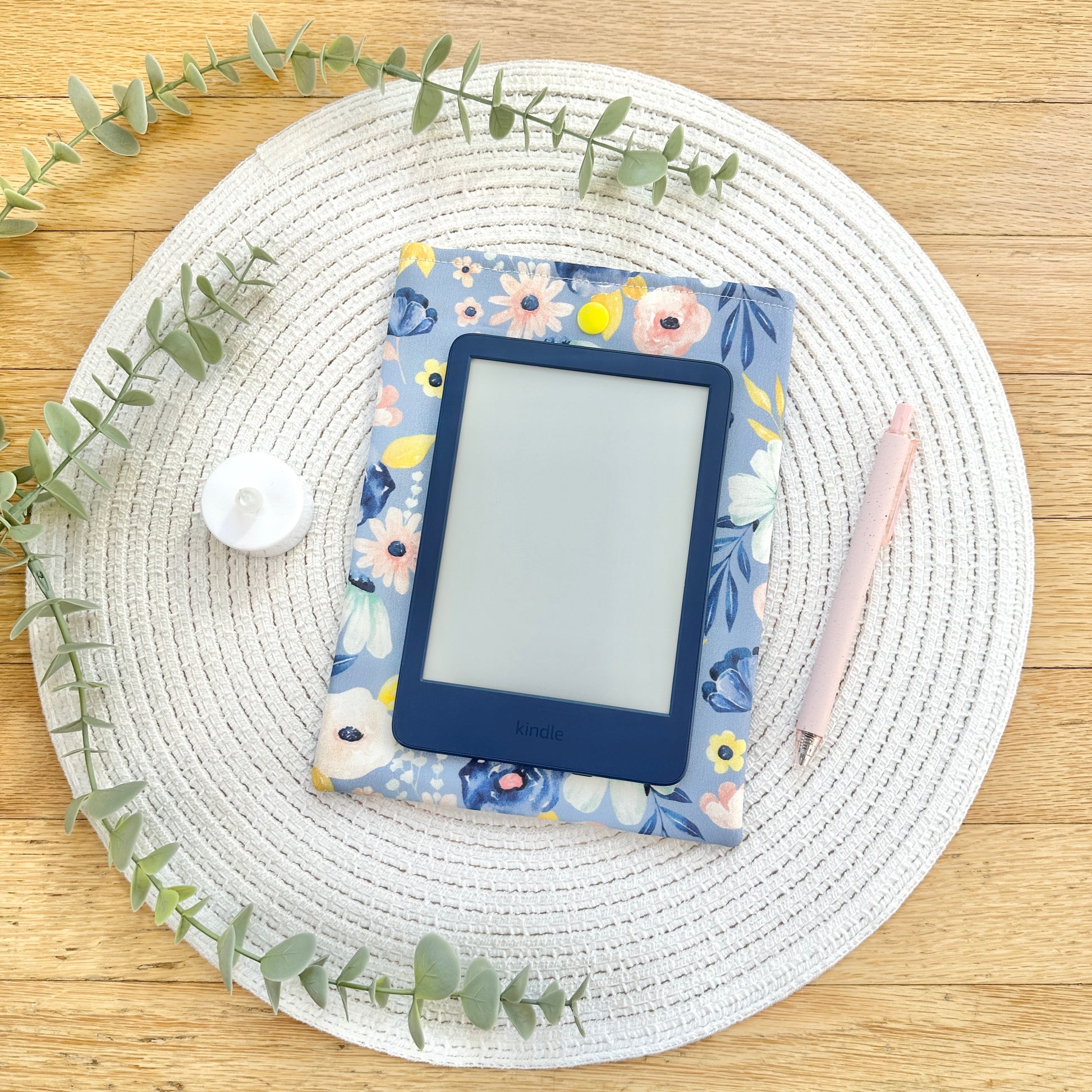 Floral-patterned e-reader cover on a wooden surface with decorative elements