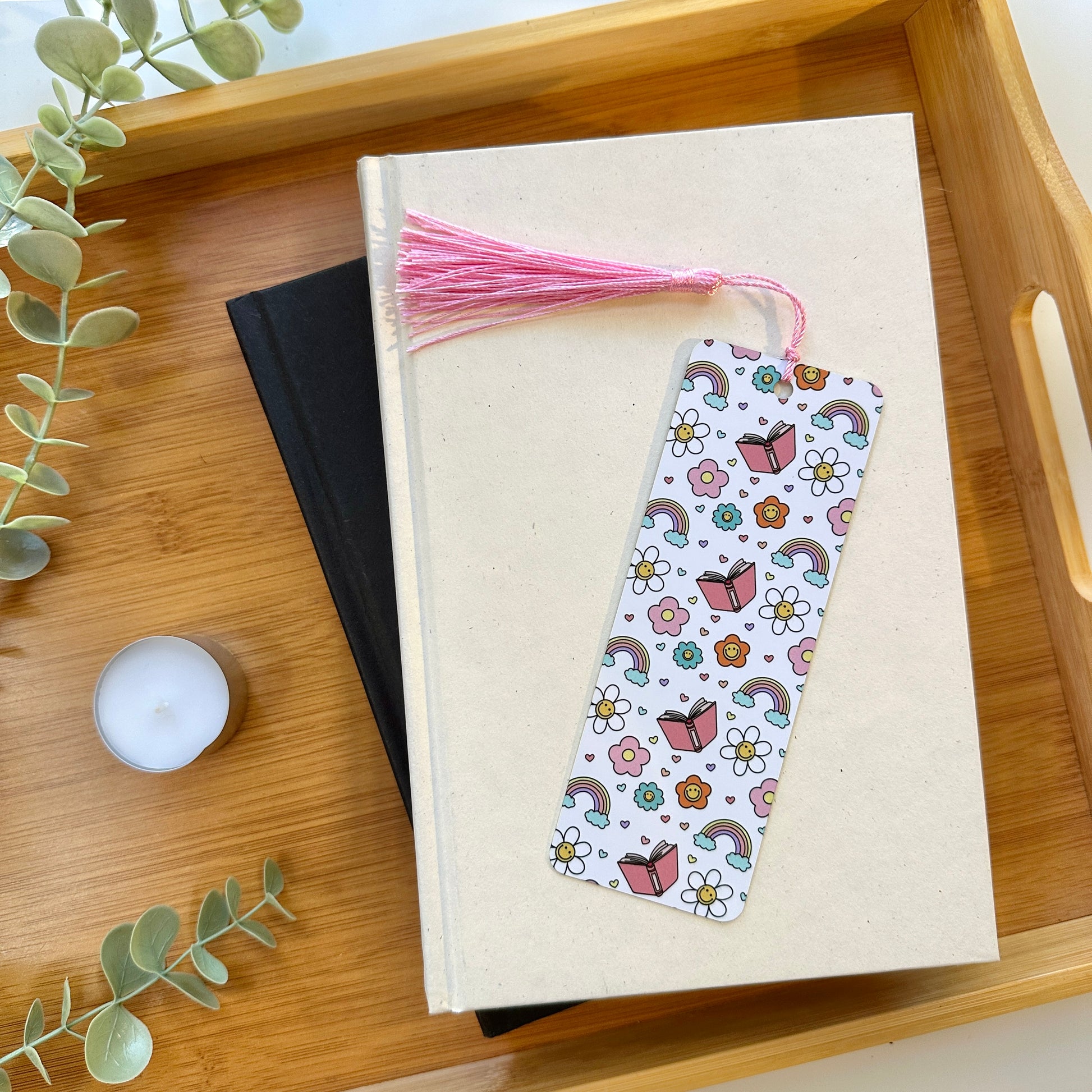 Book with a cute bookmark with tassel on a wooden tray with a candle and plant.