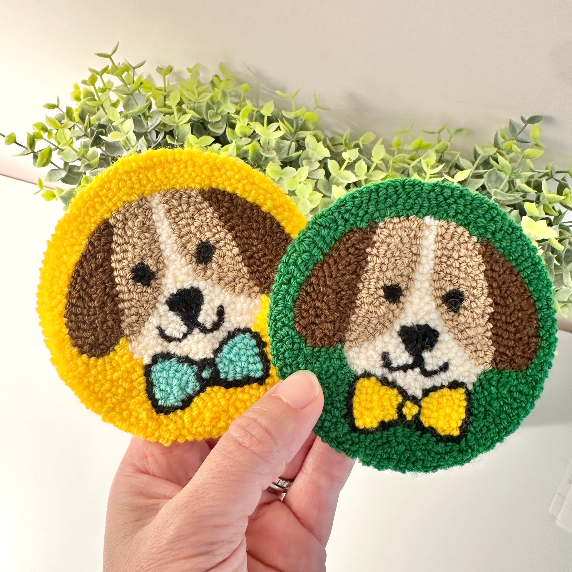 hand holding two handmade dog coasters in front of foliage