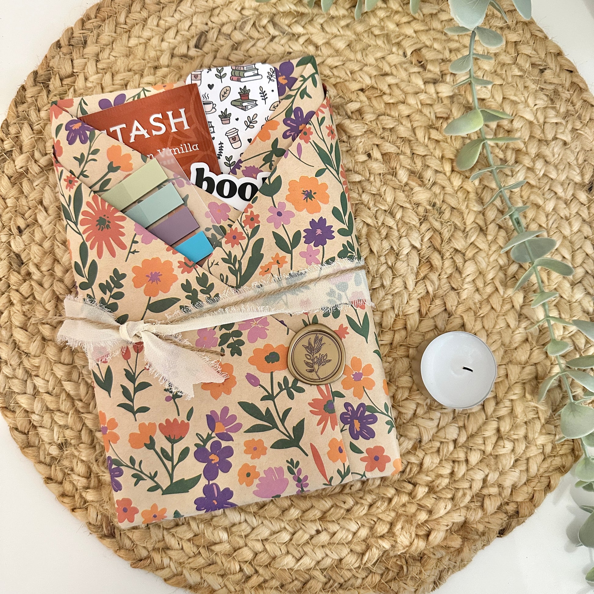 A fall-themed blind date with a book gift set displayed on a round woven straw mat with a small white candle and green leaves as props.