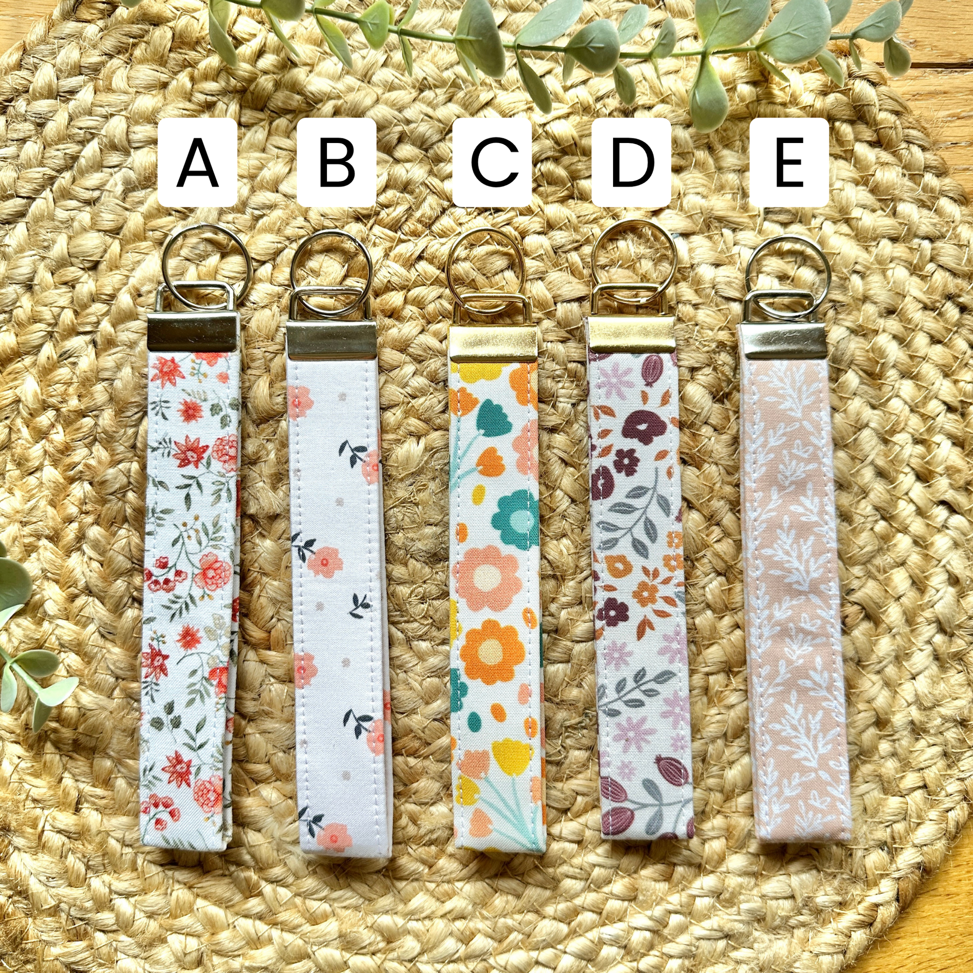 Five fall-themed wristlet keychains arranged on a woven placemat with letter A-E corresponding to the different pattern options.