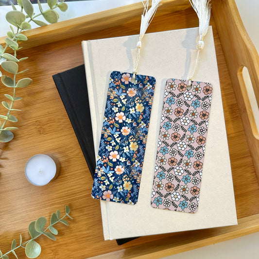 Two floral-patterned bookmarks on a book with a wooden tray and candle in the background.