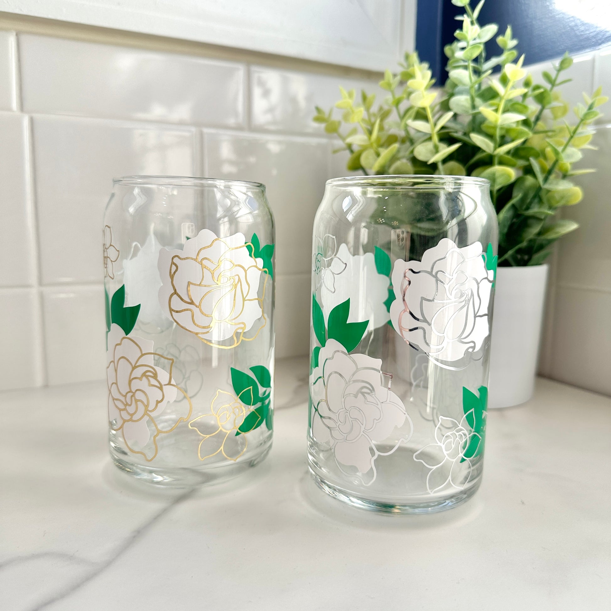 Two gardenia-patterned glass cups on a kitchen counter with a plant in the background.