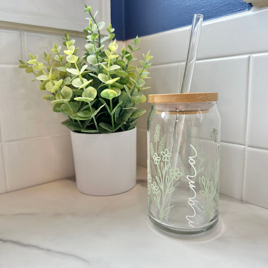 glass cup with the decorations "mama" written in cursive font and light green flowers on marble surface with green plant in the background