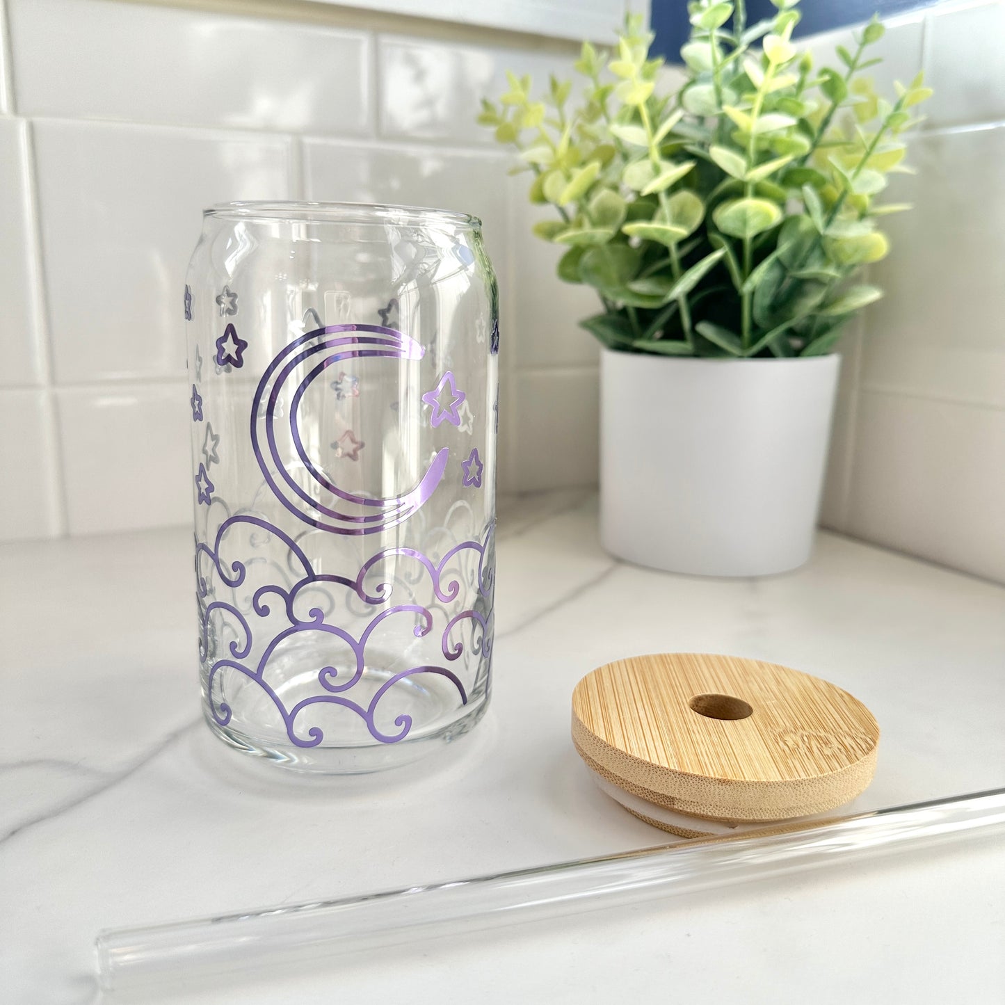 glass cup with purple holographic moon and waves design, wood top, and glass straw on kitchen counter