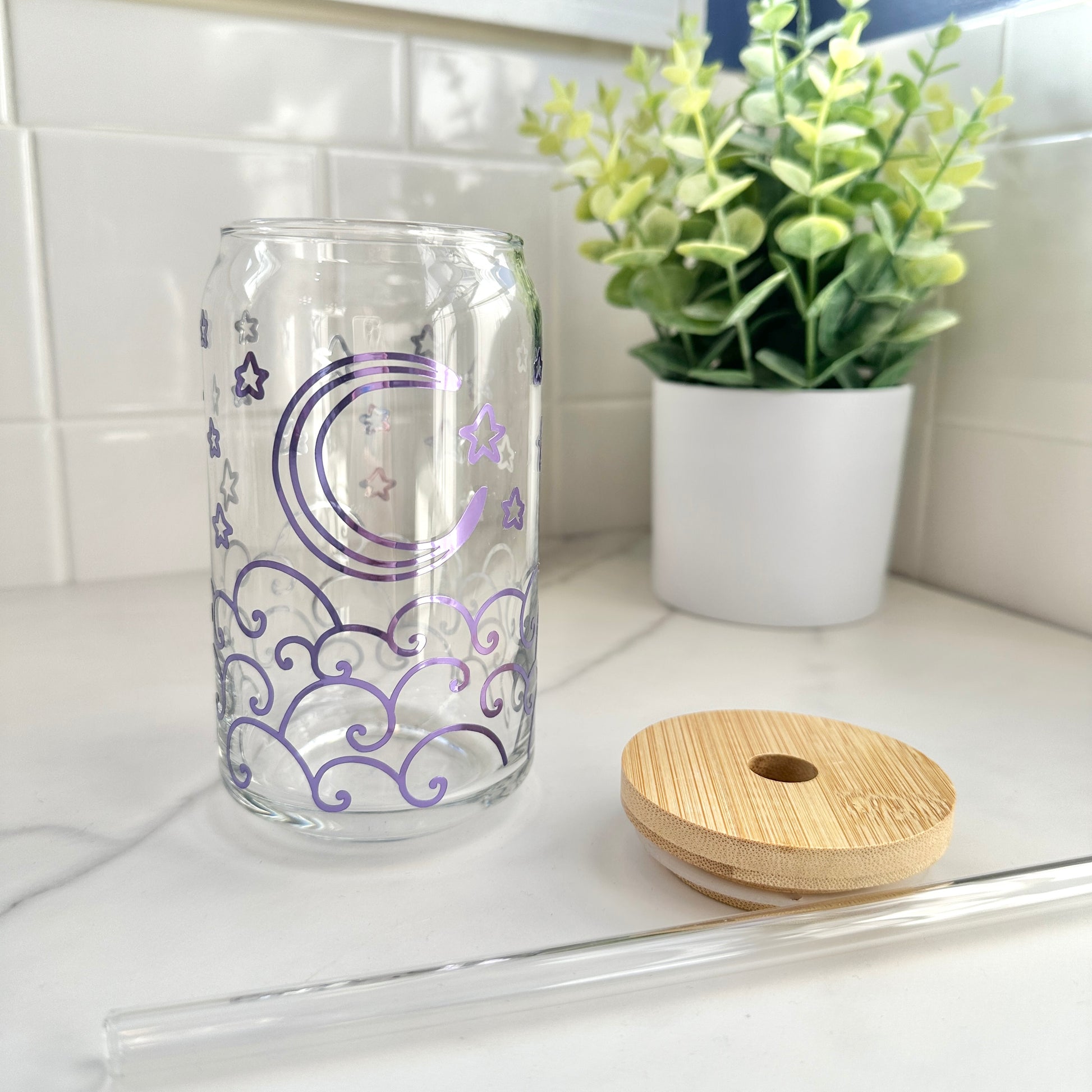 glass cup with purple holographic moon and waves design, wood top, and glass straw on kitchen counter