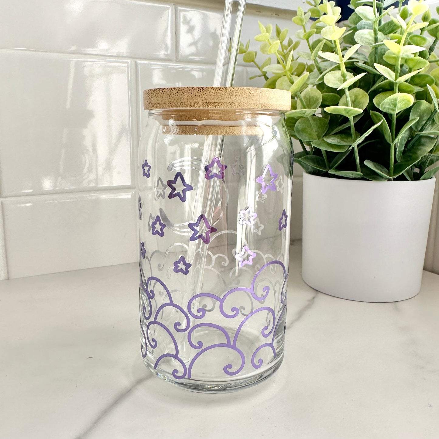 Moon and waves iced coffee glass cup on a countertop with a plant in the background