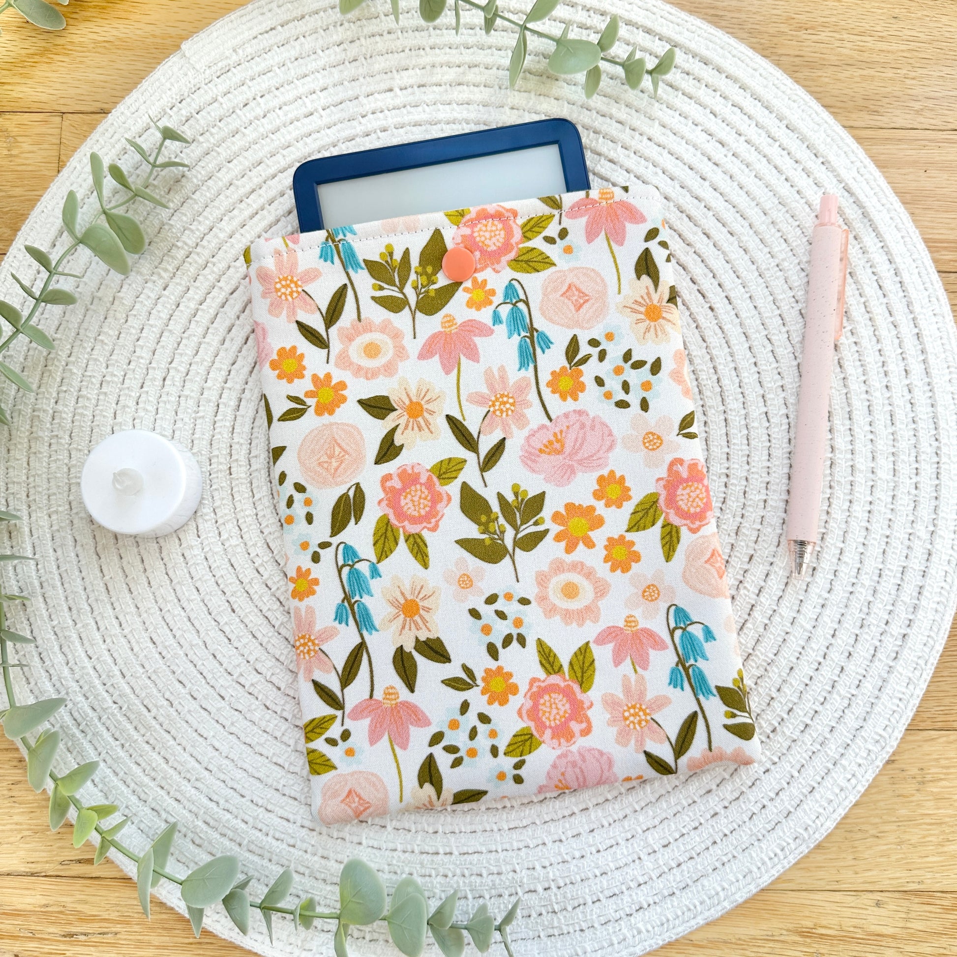 floral-patterned cotton e-reader sleeve on table with pen and candle