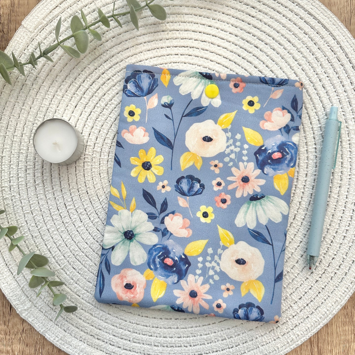 periwinkle floral-patterned e-reader sleeve on a woven mat with a candle and pen