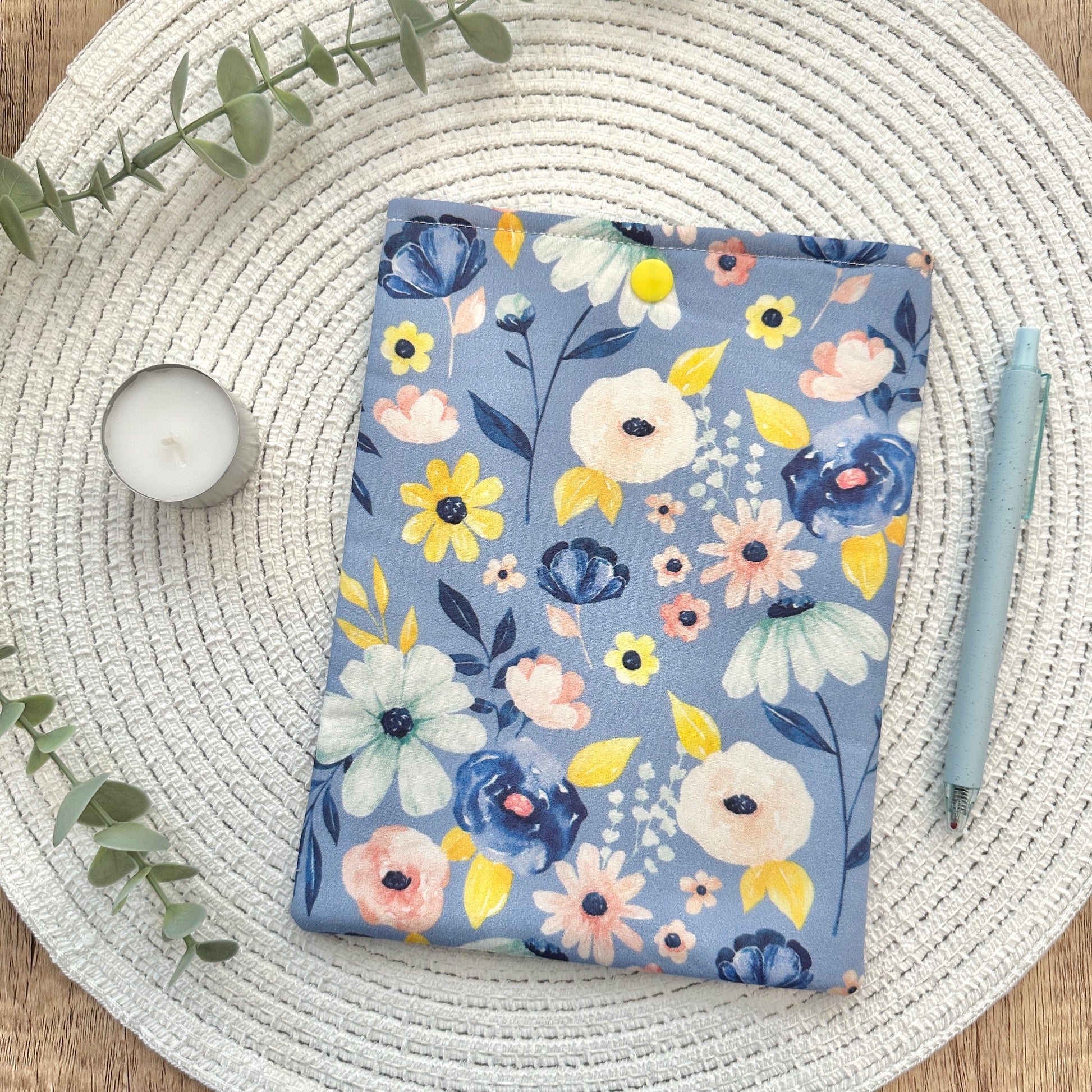 periwinkle floral-patterned e-reader sleeve on a woven mat with a candle and pen