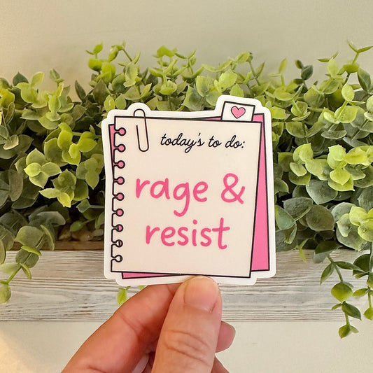 Hand holding a sticker with 'today's to do: rage & resist' text against a green plant background