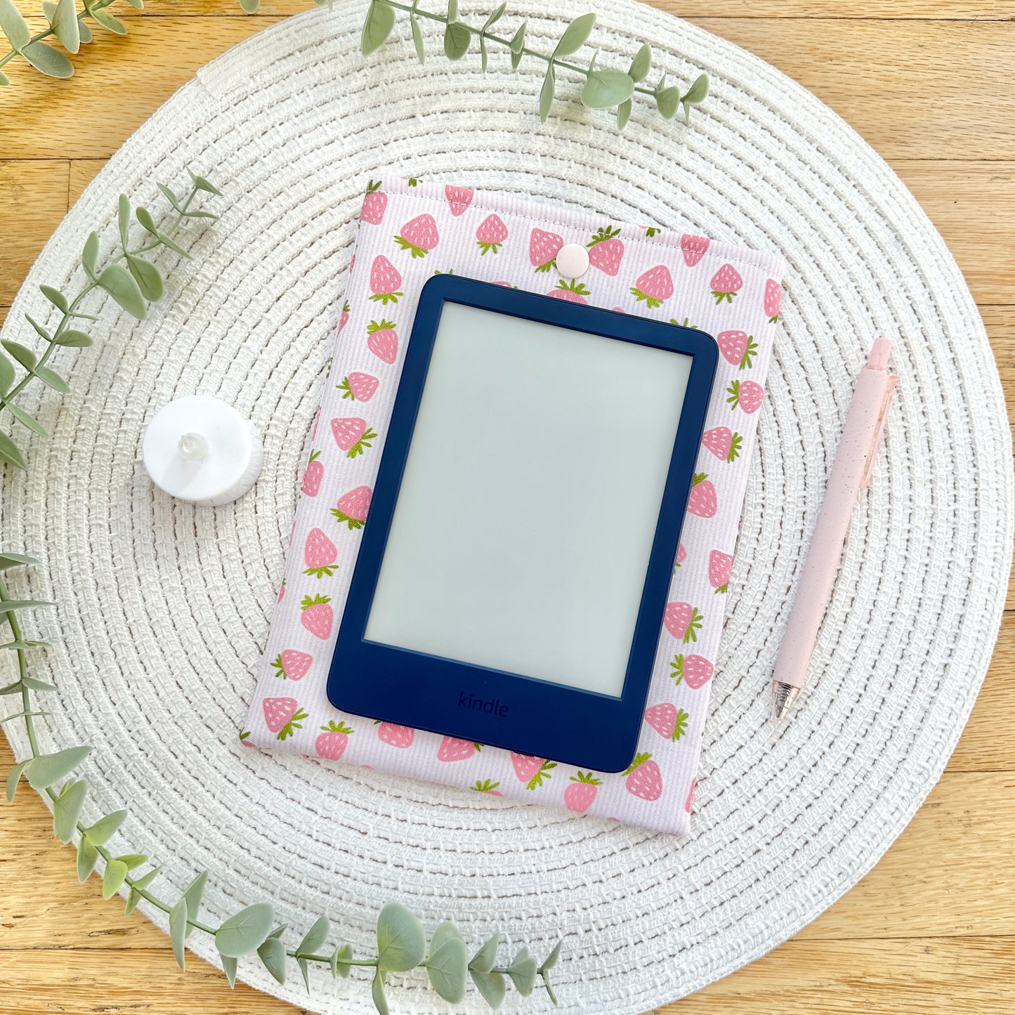 E-reader on strawberry-patterned fabric sleeve on a woven mat with green leaves