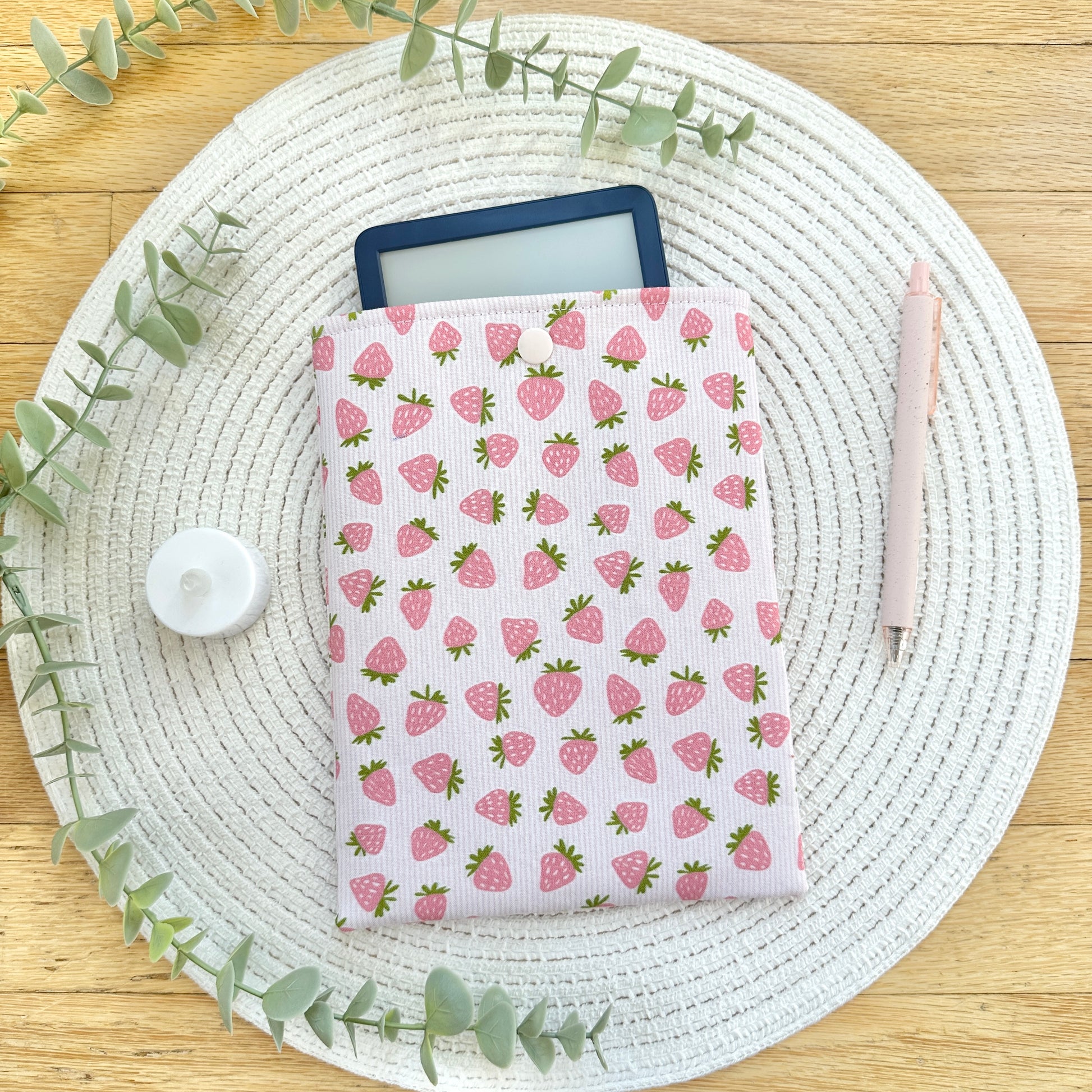 strawberry kindle sleeve on table with pen, foliage, and candle