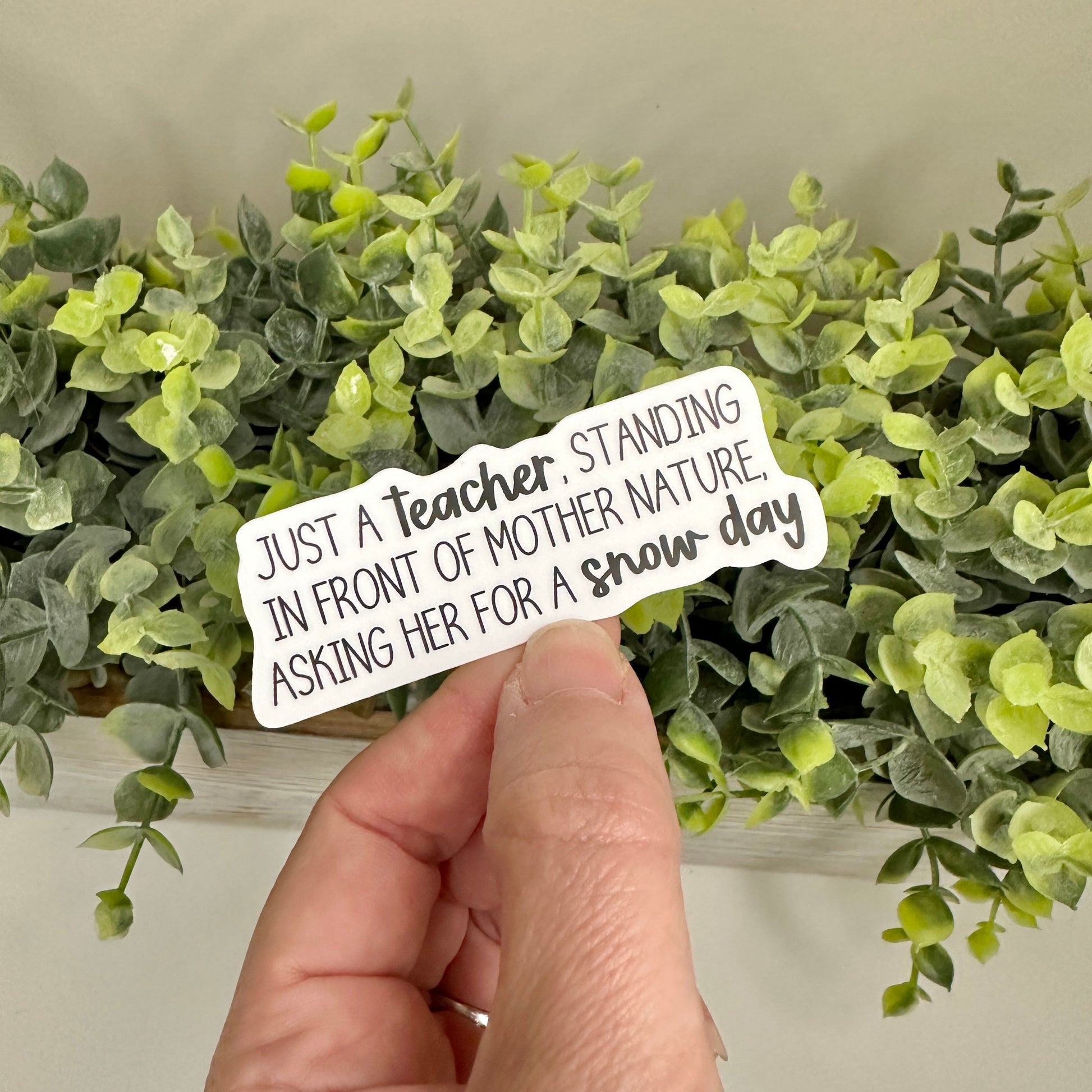 Hand holding a sticker with text in front of green plants